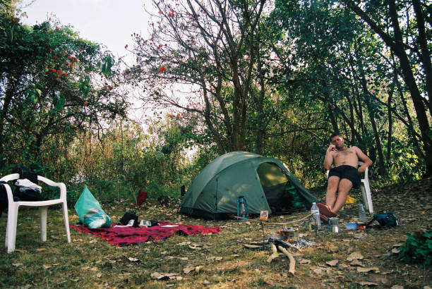 A man busy at his tent with water in a kettle boiling on a fire under trees during a Uganda camping safari